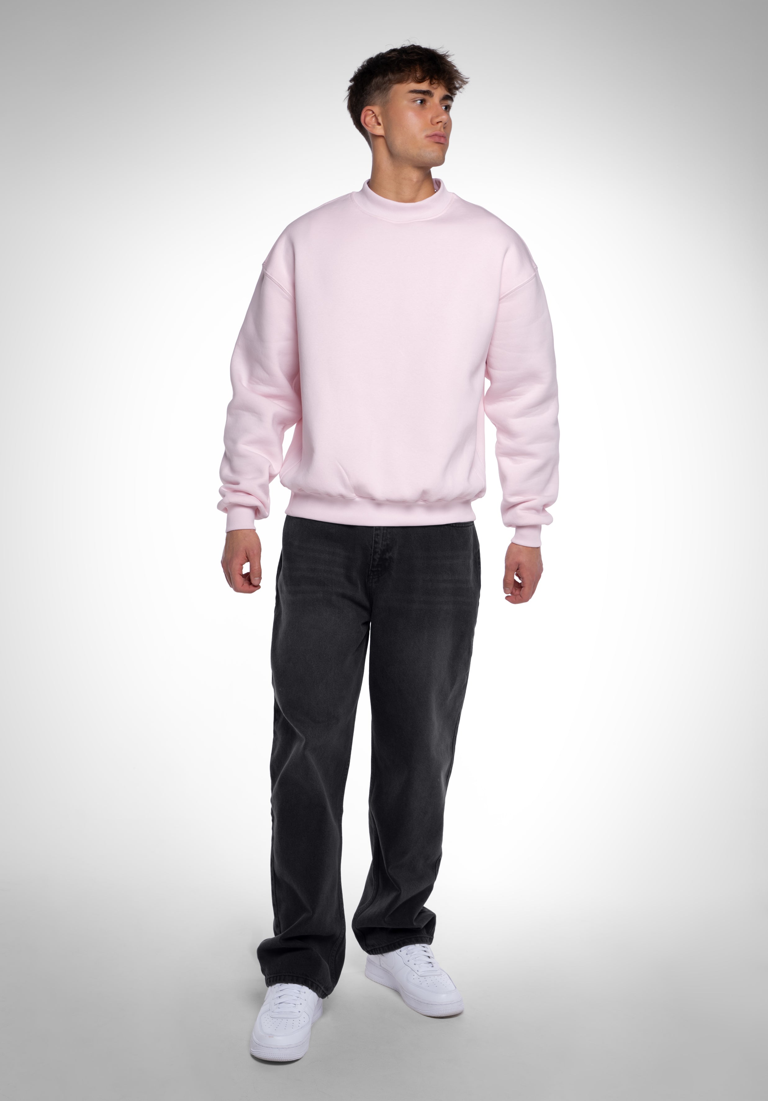 Komplettansicht eines hellrosa Oversized-Sweatshirts für Herren, kombiniert mit schwarzen Jeans und weißen Sneakern