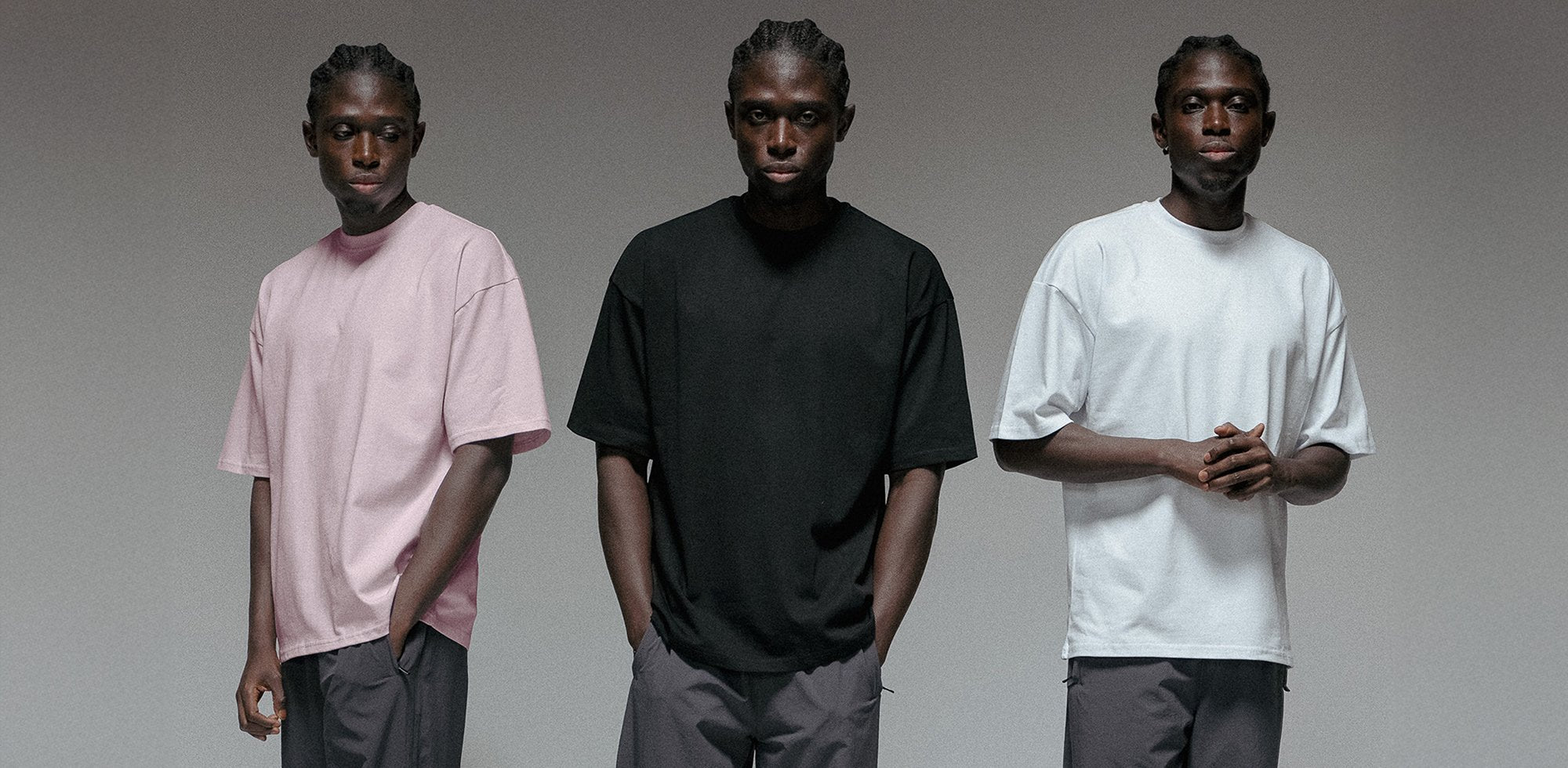 Drei Personen tragen locker geschnittene T-Shirts in Rosa, Schwarz und Weiß vor neutralem Hintergrund. Die Shirts haben einen Unisex-Schnitt und eignen sich für den Alltag.