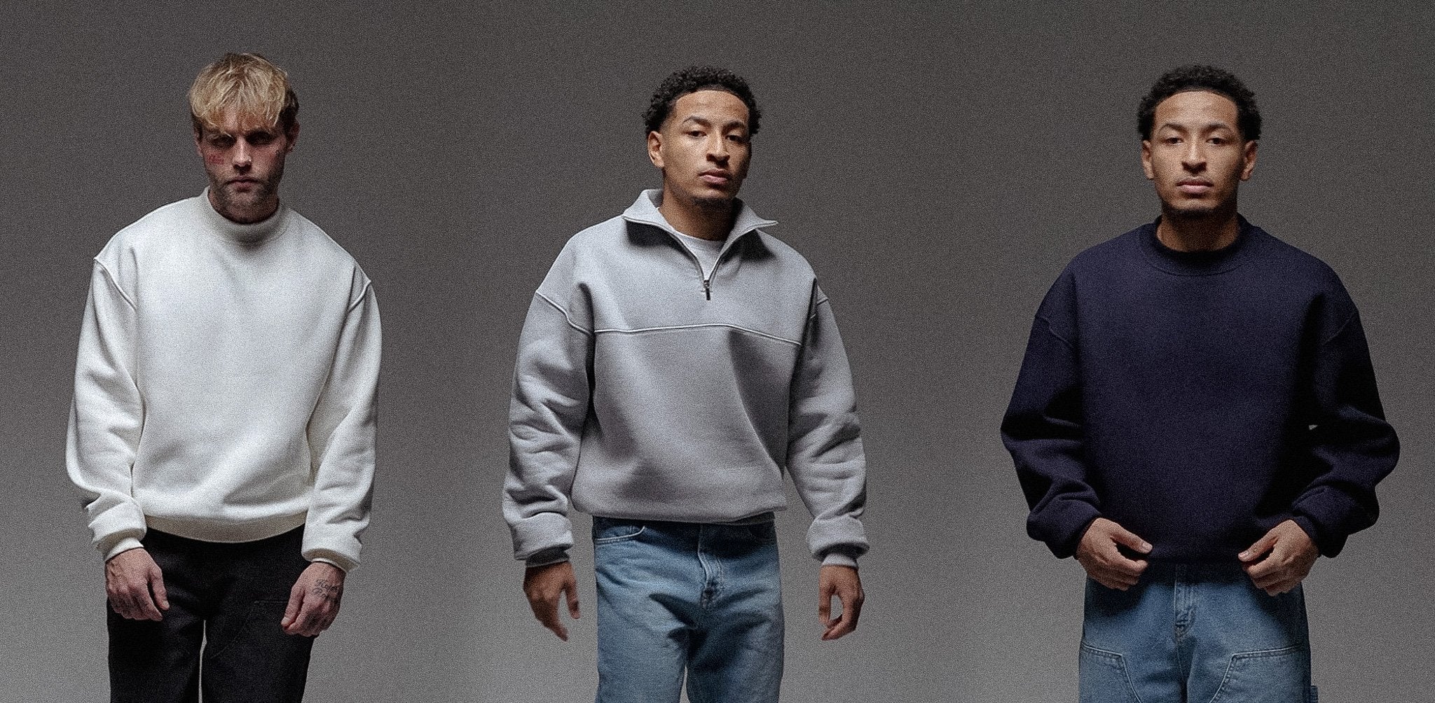Drei Männer tragen Sweater aus dickem Material in Off-White, Hellgrau und Dunkelblau. Die Passformen sind entspannt und für kühlere Temperaturen geeignet.